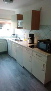 eine Küche mit weißen Schränken, einer Spüle und einer Mikrowelle in der Unterkunft Kleines Apartement zwischen Ega und Messe Erfurt in Erfurt