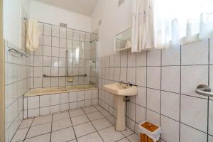 a white tiled bathroom with a sink and a tub at Old Coach Road Guest House in Barberton