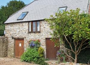 a stone house with a wooden door and flowers at Red Doors Farm Cottages in Honiton