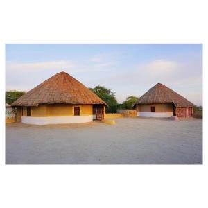 two buildings with thatched roofs in a field at Shaam E Sarhad Resort in Bherandiāla