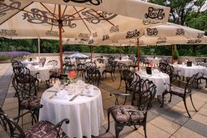 ein Restaurant mit weißen Tischen, Stühlen und Sonnenschirmen in der Unterkunft La Contessa Castle Hotel in Szilvásvárad