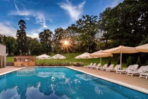 uma piscina com cadeiras brancas e guarda-sóis em La Contessa Castle Hotel em Szilvásvárad