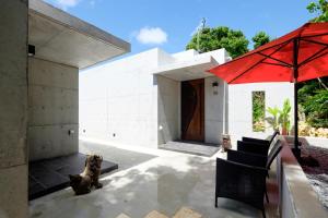 a house with a red umbrella and two cats sitting on a patio at Kaiza in Nanjo