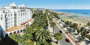 a beach with palm trees and a building and the ocean at La Collina di Emma in Massignano