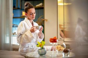 a woman in a robe holding a cup of coffee at Grand Poet Hotel and SPA by Semarah in Rīga