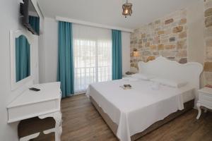 a bedroom with a white bed and a stone wall at Alesya Otel in Çiftlikköyü