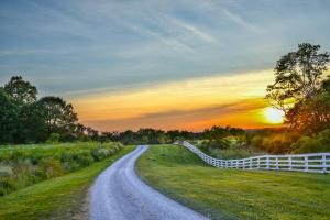 une route de campagne avec une clôture blanche au coucher du soleil dans l'établissement Shaker Village of Pleasant Hill, à Harrodsburg