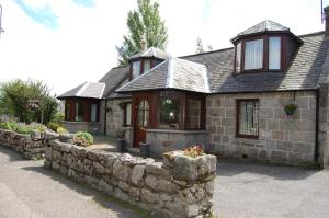 a stone house with a stone retaining wall at Applegrove B&B in Boat of Garten