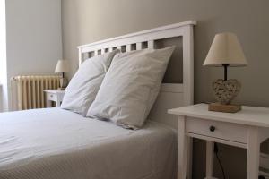 Cama con almohadas blancas y mesa con lámpara en La Folie des Remparts, en Carcassonne