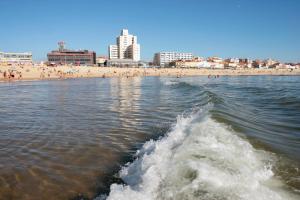 a wave in the water with a beach and buildings in the background at Hotel Apartamento Solverde in Espinho