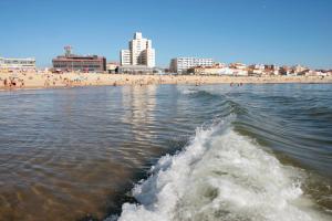 een golf in het water met een strand en gebouwen op de achtergrond bij Hotel Apartamento Solverde in Espinho