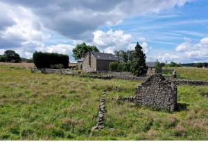 eine alte Steinmauer in einem Feld mit einem Haus in der Unterkunft Cuckoostone Barn in Buxton