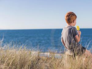 un joven parado en la playa sosteniendo un plátano en Pacific Park Christian Holiday Camp, en Papamoa