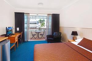 Habitación de hotel con cama, escritorio y balcón. en City Oasis Inn, en Townsville
