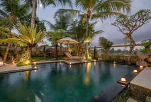 an infinity pool with palm trees and an umbrella at Prabhu Ubud Villa in Ubud