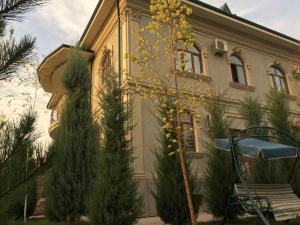 ein Haus mit Bäumen und einer Bank davor in der Unterkunft Mavie Guest House in Taschkent