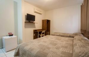 a bedroom with two beds and a tv on the wall at Hotel Maraja in Uberlândia