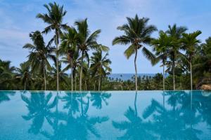 une piscine avec des palmiers et l'océan en arrière-plan dans l'établissement Taj Green Cove Resort and Spa Kovalam, à Kovalam