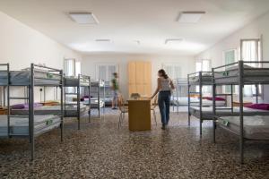 kobieta przechodząca przez pokój z łóżkami piętrowymi w obiekcie Ostello Bassano Del Grappa w mieście Bassano del Grappa