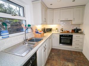 eine Küche mit weißen Schränken und einer Spüle und einem Fenster in der Unterkunft Woodleigh Cottage in Ballycastle + 23 Fotos