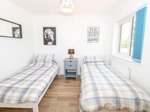 two beds in a room with a table and a window at 6 Yarmouth Cottages in Freshwater