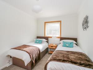 two beds in a room with white walls and blue pillows at Cromallt in Aberfeldy