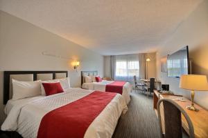 Cette chambre d'hôtel comprend 2 lits avec des draps rouges et blancs. dans l'établissement Chateau Roberval, à Roberval