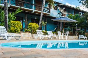 a swimming pool with white chairs and an umbrella at Pousada Recanto da Serra in Serra do Cipo