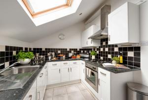 eine Küche mit weißen Schränken und schwarzen Fliesen an der Wand in der Unterkunft Fishermans Warehouse in Whitby