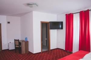 a room with red curtains and a desk and a tv at Pensiunea Iliada in Sibiu