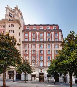 um grande edifício de tijolos vermelhos com árvores em frente em Hotel Hernán Cortés em Gijón