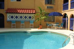 einen Pool mit Stühlen, einem Tisch und einem Sonnenschirm in der Unterkunft Sevilla Inn Kissimmee- Near Disney in Kissimmee