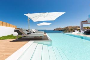 una piscina con una sombrilla blanca y sillas y una piscina en Wave Villa, Seaside Living & Your Own Beach Spot, By ThinkVilla, en Panormos Rethymno