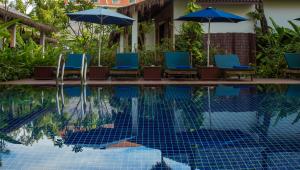 a swimming pool with blue chairs and umbrellas at La Rivière d' Angkor Resort in Siem Reap