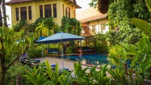 a pool with an umbrella and chairs and a house at La Rivière d' Angkor Resort in Siem Reap