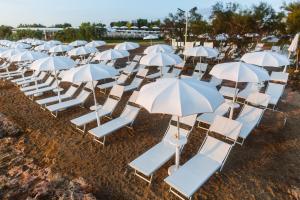 a row of white chairs and umbrellas on the beach at Torre Cintola Greenblu Sea Emotions in Monopoli