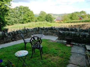 two chairs and a table in a yard with a stone wall at Pell Dell Apartment in Holmfirth
