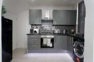 een keuken met grijze kasten en een wasmachine en droger bij Burton House in Leeds