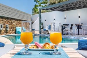 two glasses of orange juice on a table next to a swimming pool at Lithos Luxury Suites in Tinos