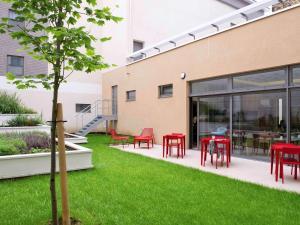 un jardin avec des tables et des chaises rouges à côté d'un bâtiment dans l'établissement Aparthotel Adagio Paris Vincennes, à Vincennes