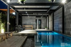 a swimming pool with a patio and a house at Owl Poshtel Kanchanaburi in Kanchanaburi