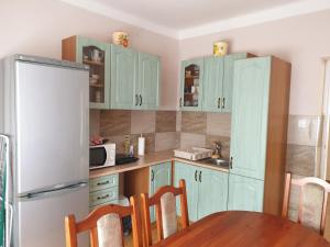 La cuisine est équipée d'armoires vertes, d'une table et d'un réfrigérateur. dans l'établissement Edina apartman, à Balatonlelle