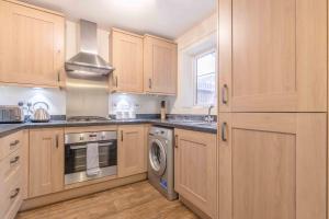 cocina con armarios de madera, lavadora y secadora en WINDSOR 10 MINS - 3 DOUBLE BEDROOM & 2 BATHROOM HOUSE WITH PARKING, en Slough
