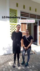 dos personas están de pie en frente de un edificio en LG Homestay en Kepanjen