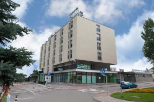 un edificio blanco alto en una calle con aparcamiento en Hotel Gromada Łomża, en Łomża