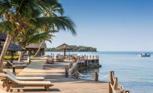 a dock with chaise lounges and palm trees on a beach at Corail Noir Hotel in Ambaro
