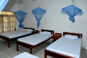 three beds in a room with blue umbrellas on the wall at New Land Guest House in Pasikuda