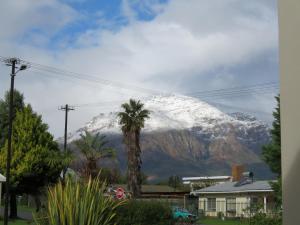 a snow covered mountain with a palm tree and a house at Koraalboom Guesthouse in Wolseley