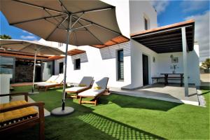 a patio with chairs and an umbrella and grass at Holiday House and Spa Lanzarote in Tías