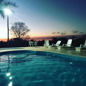 una piscina con sillas y una puesta de sol en el fondo en Pousada e Restaurante Valle dos Ventos, en Chapada dos Guimarães